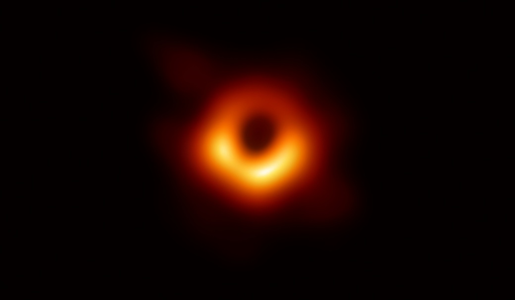 The first direct image of a black hole: a small, soft ring of orange light around a dark centre.