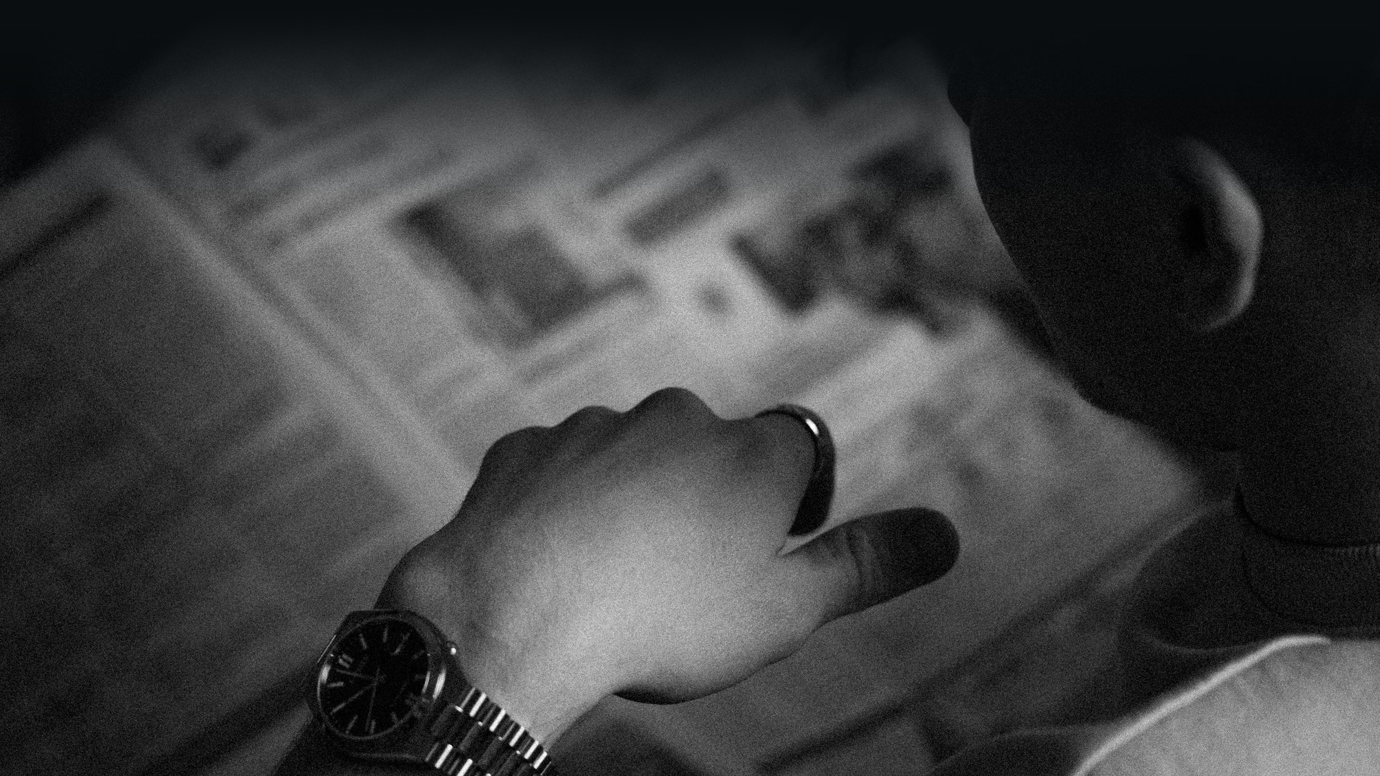 Someone reading a newspaper, checking a wristwatch.