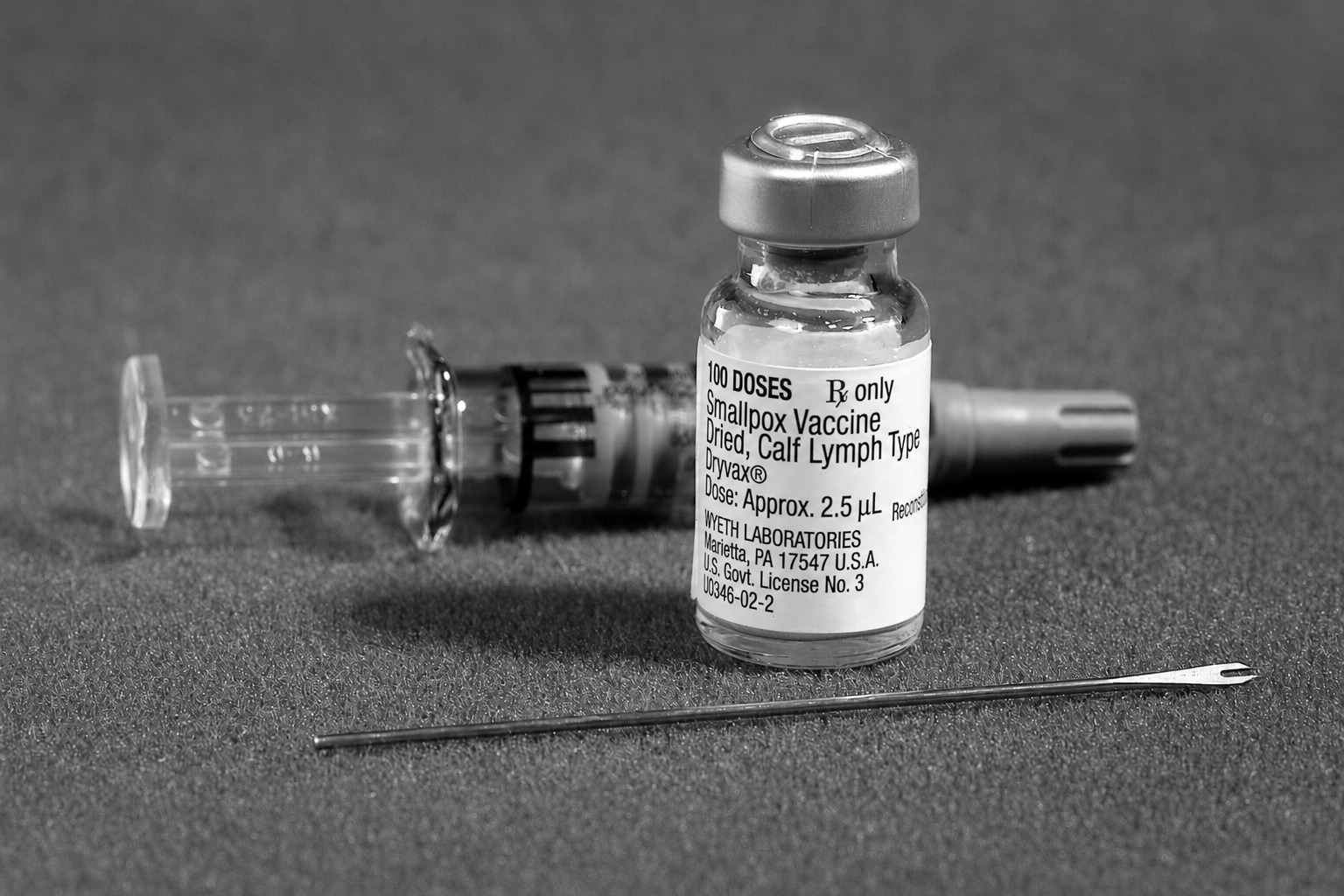 A vial of freeze-dried smallpox vaccine beside a syringe and a bifurcated needle.